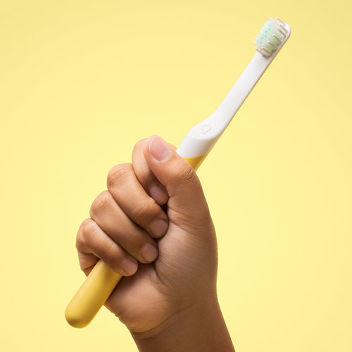 A child's hand holding a yellow and white sonic toothbrush with a blue brush head.