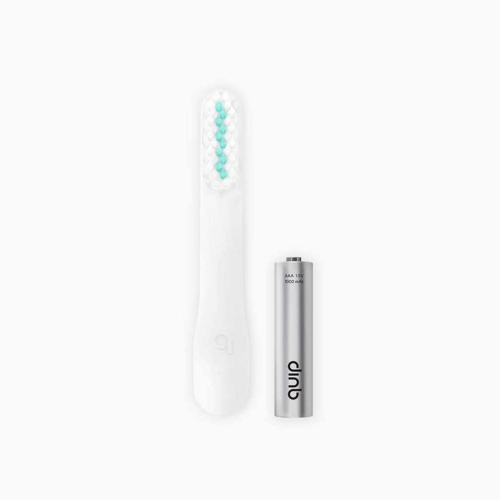 An image showing a white electric toothbrush head refill with soft bristles and a tongue scraper, accompanied by a AAA battery.